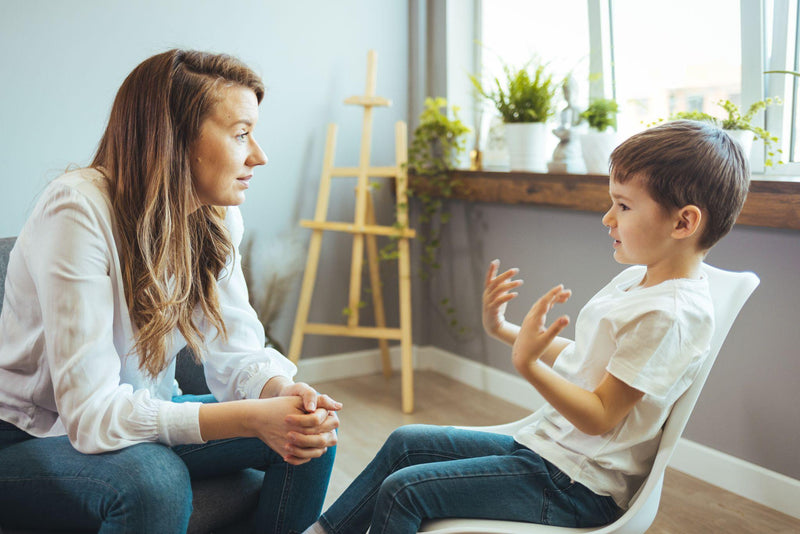 Young female school psychologist having serious conversation with smart little boy